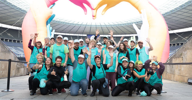 Das gesamte Team des Walking Acts posiert für ein Gruppenbild vor dem Emblem der Special Olympic World Games am Eingang zum Olympia Stadion