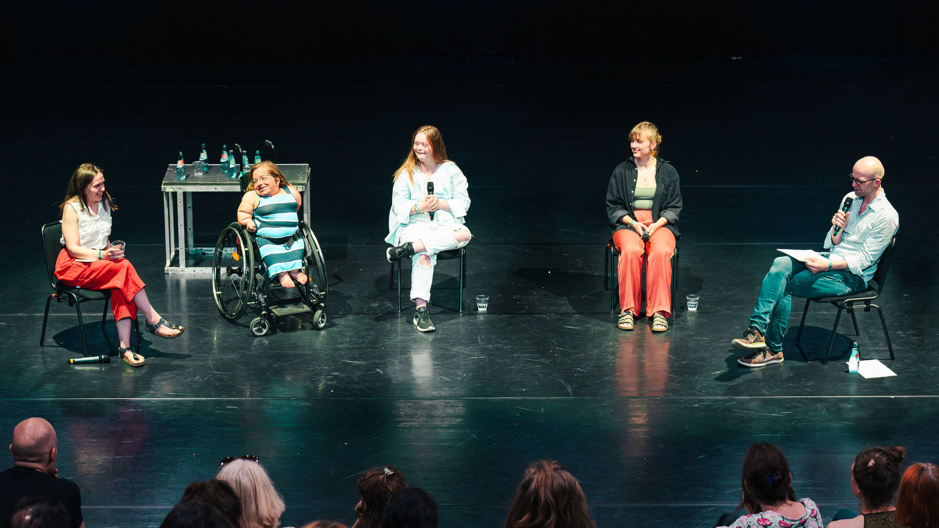 Auf der Bühne der fabrik Potsdam sitzen von links nach rechts die Panelist*innen des Panels „Was bedeutet Inklusion in der Schauspielausbildung?“  Alrun Hofert, Jana Zöll, Amelie Gerdes, Hanna Frank und der Moderator Georg Kasch vor einem Publikum. Alrun Hofert spricht gerade und lächelt dabei.