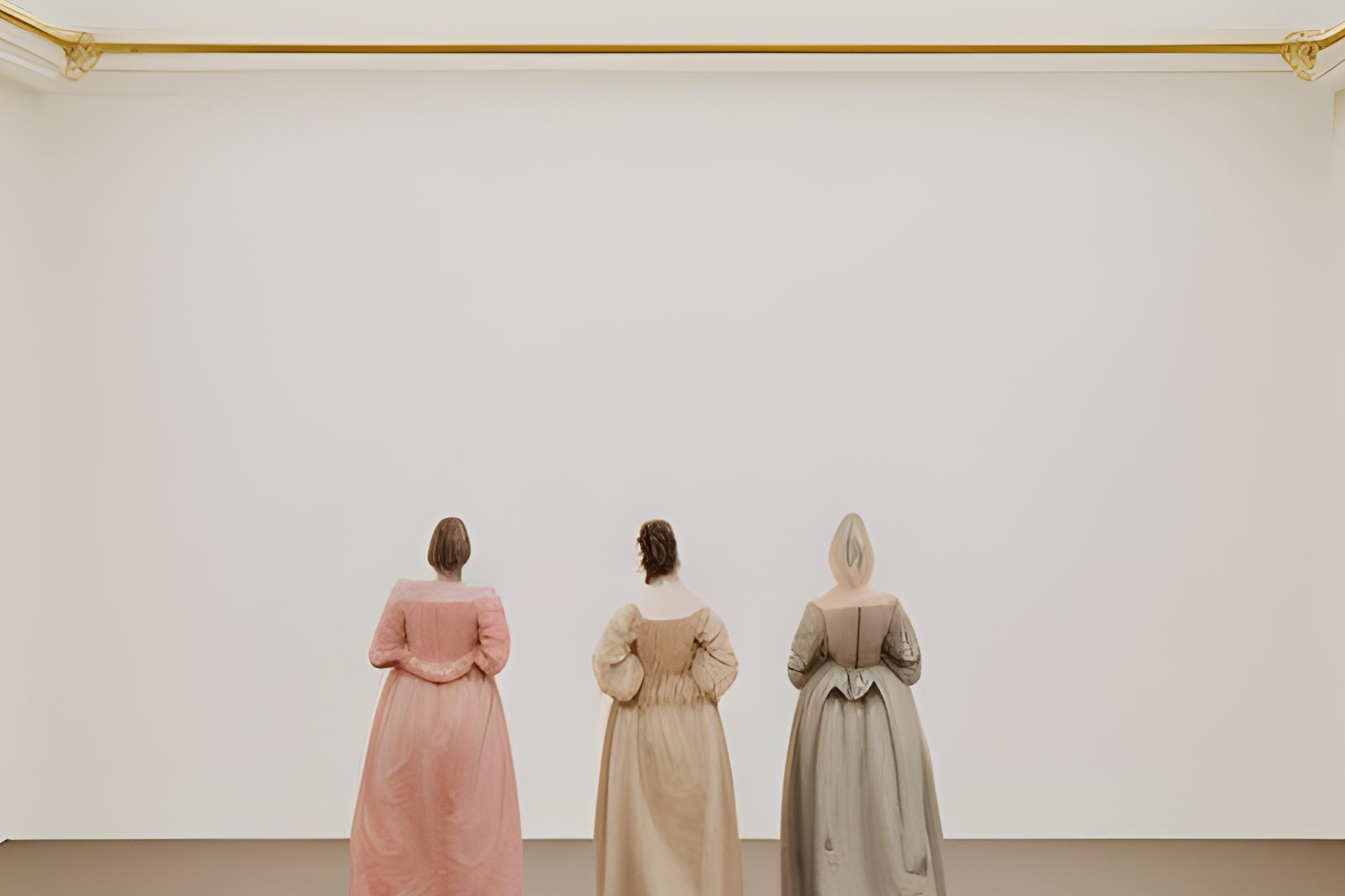 Drei Personen in bodenlangen, pastellfarbenen Kleidern mit dem Rücken zum Betrachter in einem weißen, hellen Raum 