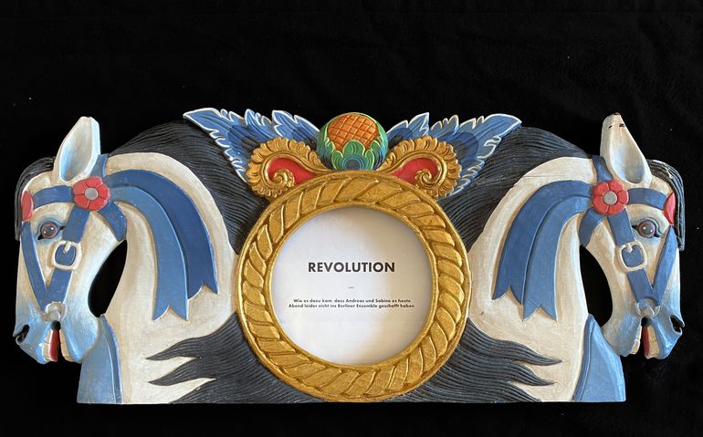Schriftzug "Revolution" umrahmt von einem runden Goldrahmen und zwei bemalten Holzpferden 