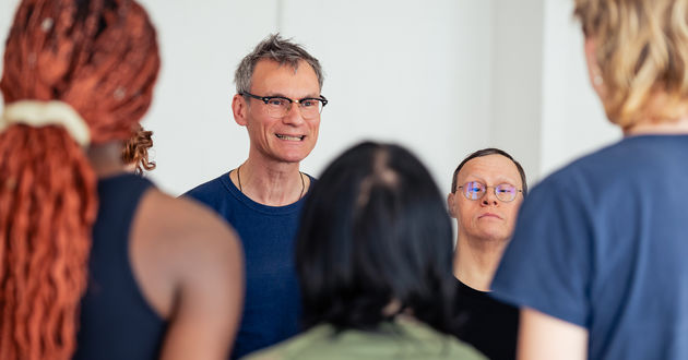 Die Teilnehmenden des Grundlagenkurses an der UdK stehen in einem Proberaum im Kreis. Mit konzentriertem Blick geradeaus, erklärt Prof. Enrico Stolzenburg etwas. Neben ihm steht Michael Wittsack, Ensemblemitglied am RambaZamba Theater, und hört zu.