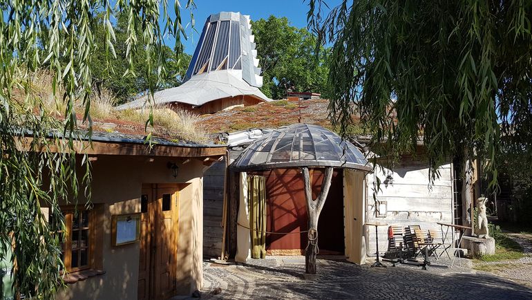 Foto des Eingangsbereichs des "Theater am Rand", Zollerbrücke, im Sommer umgeben von Bäumen 