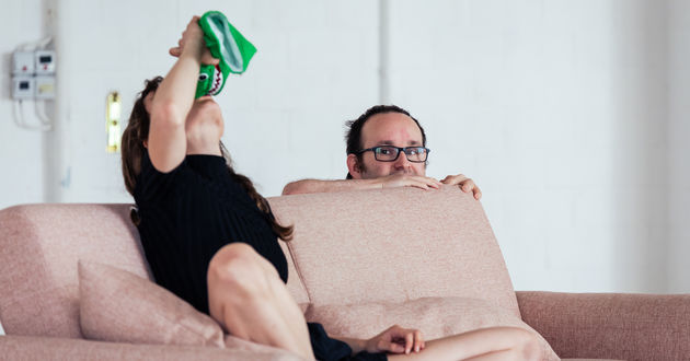 Bei einer 2 Personen Improvisation sitzt die eine Figur auf einem  Sofa. Sie hat den Kopf in den Nacken gelegt und hält sich eine grüne Krokodil-Handpuppe über den Mund, als würde sie daraus trinken. Hinter dem Sofa versteckt sich die andere Figur und schaut der ersten Figur beim Trinken zu. 