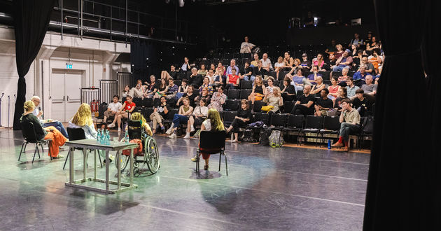 Auf der großen Bühne der fabrik Potsdam sitzen von rechts nach links die Panelist*innen Alrun Hofert, Jana Zöll, Amelie Gerdes, Hanna Frank und der Moderator Georg Kasch mit dem Rücken zur Kamera. Sie sprechen zu einer vollen  Zuschauer*innentribüne.